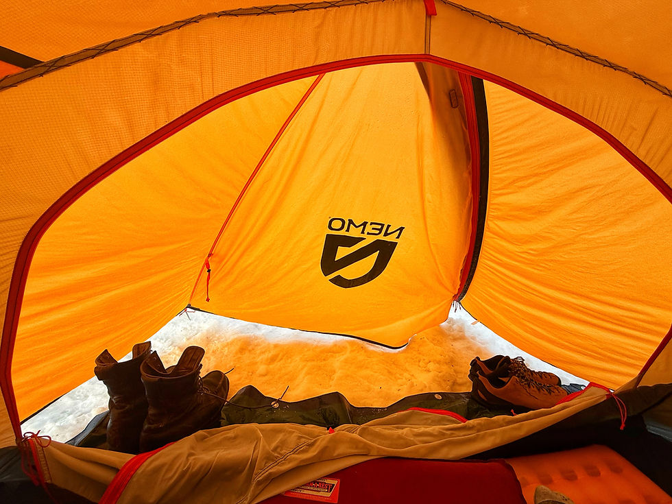 Inside a yellow tent, boots and shoes rest on snow. The tent is labeled with "NEMO." Cozy and warm atmosphere.