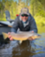 fly angler in camo hat and sunglasses holding a large brown trout