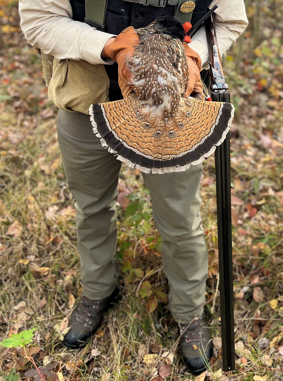 hunter in boots holding shotgun and ruffed grouse