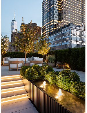 An aluminum and wood clad water feature lit up as the sun goes down over this luxury NYC rooftop garden.