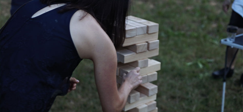 Frau zieht bei einem Teamspiel einen Klotz aus einem Riesen-Jenga-Spiel