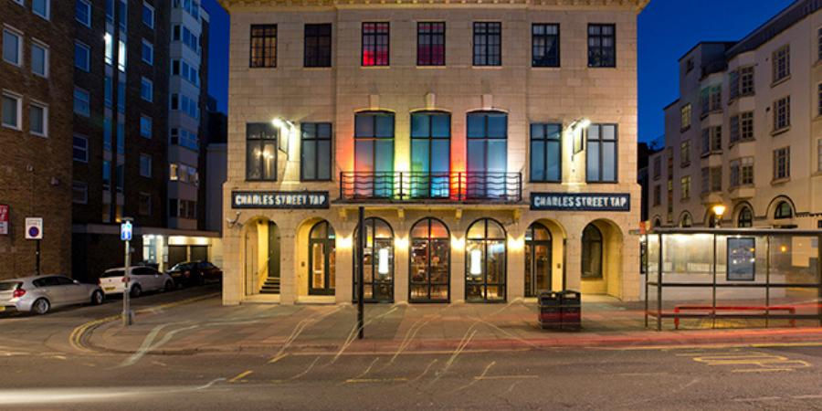 Eye-level view of a quiet Brighton pavement outside a closed nightlife venue with rainbow bunting in a nearby window.