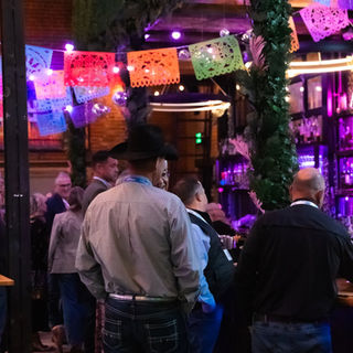 Crowd at the COATI bar under neon signs and colorful papel picado