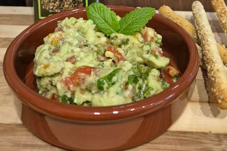 A bowl with pea, avocado and mint dip and breadsticks beside it.