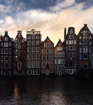 Classic Amsterdam canal houses at sunset with water reflections. Iconic Dutch architecture in the evening light,  cityscape photography