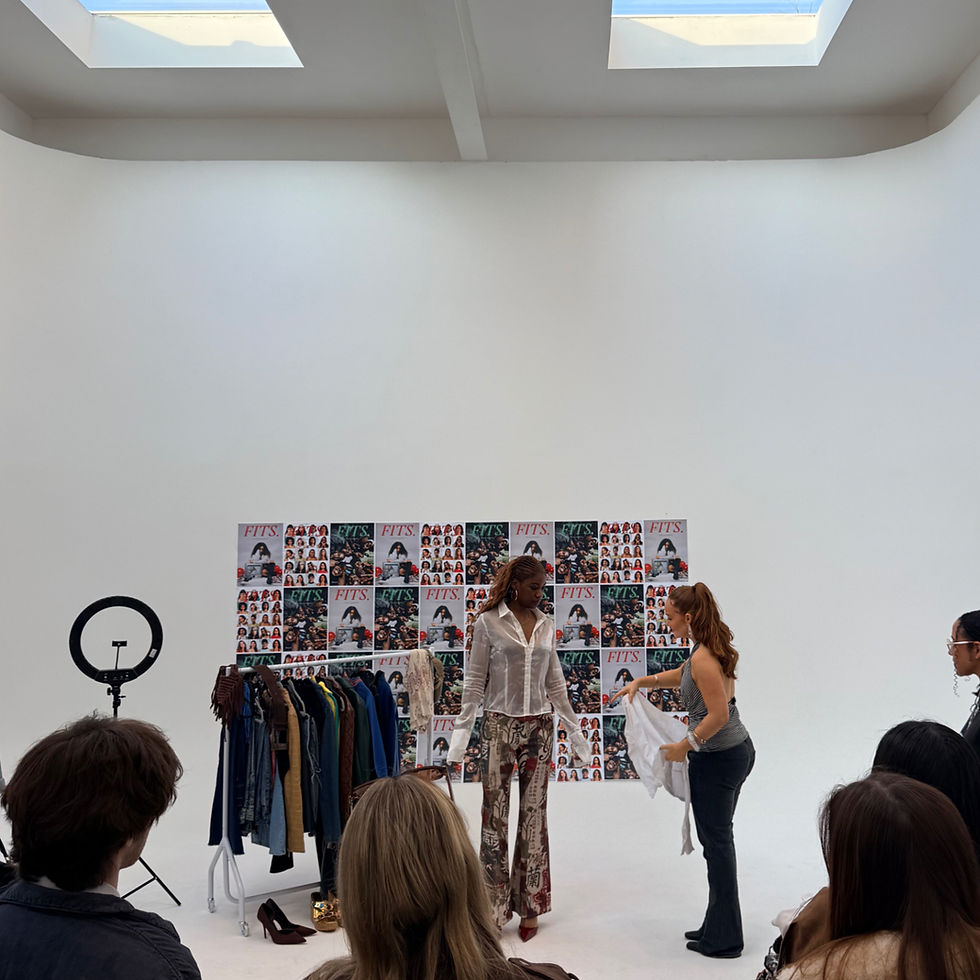 Fashion workshop in manchester studio. A woman showcases clothes to an audience. Background features colorful "FITS" magazine covers. Bright setting.