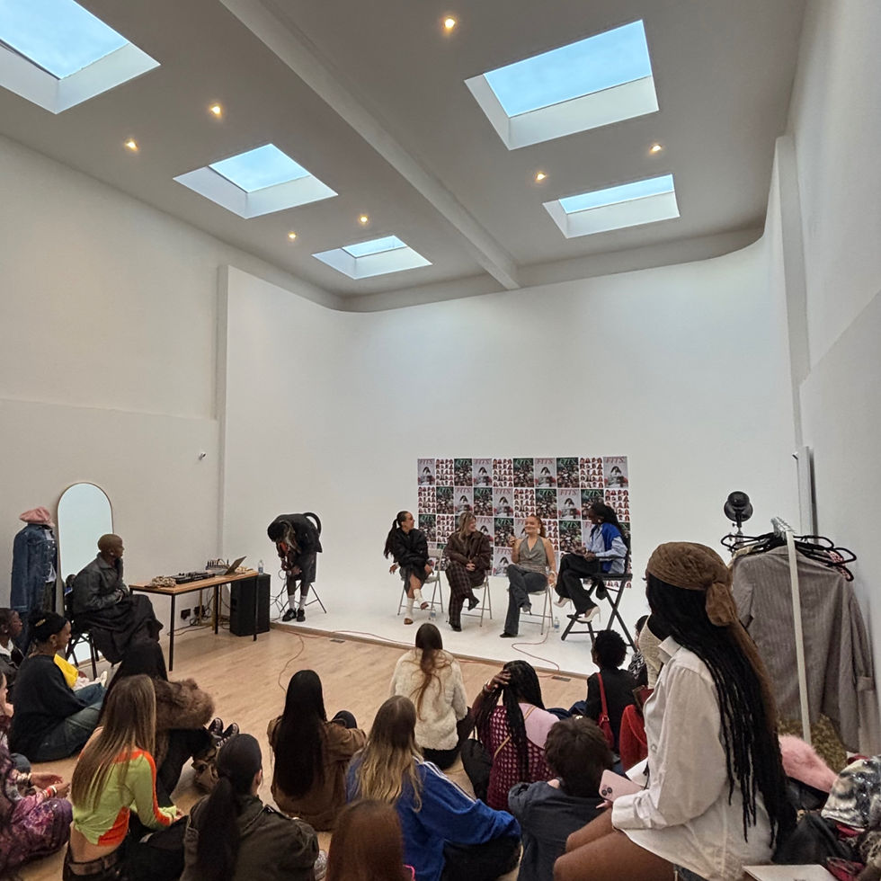 Panel discussion with five people seated in a bright room with skylights. An audience listens attentively; colorful posters on the wall.