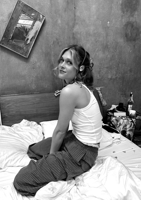 Sängerin Anaïs kniet auf einem ungemachten Bett und schaut über die Schulter in die Kamera.