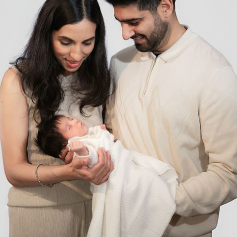 Couple smiling at their newborn baby in a white wrap.