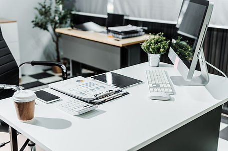 A modern, white-colored business office with a wooden desk, calculator, desktop computer,