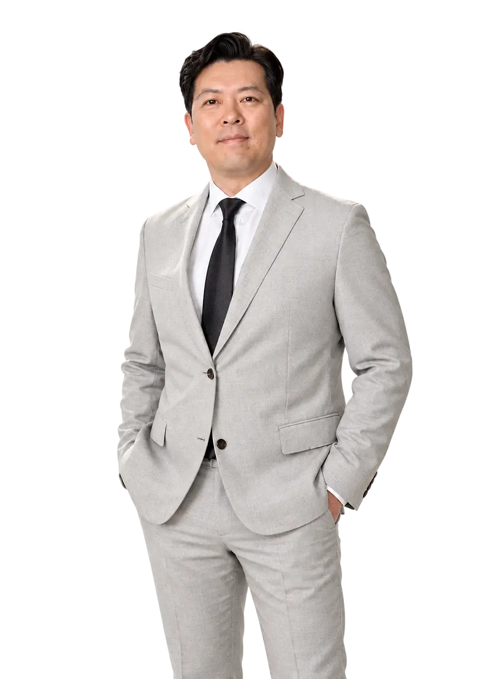 Studio photography of a businessman in a light grey suit. He stands confidently with his hands in his pockets against a black backdrop.