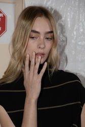 Backstage image of a model with tousled hair in a black coat from Proenza Schouler's collection, complemented by an elegant nude manicure by Sofie Roth
