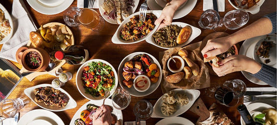 A traditional Georgian dinner: a table filled with a variety of national dishes, including khinkali, vegetable salads, pastries, and glasses of wine, with guests gathered around