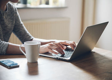 Person typing on laptop, coffee cup and phone on wooden table background.