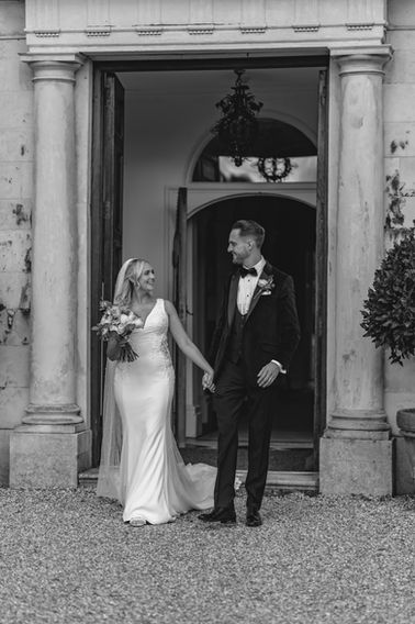 Bride and groom at the entrance doors of Braxted Park, Essex, with a white bridal bouquet by Rosie Obeney Flowers