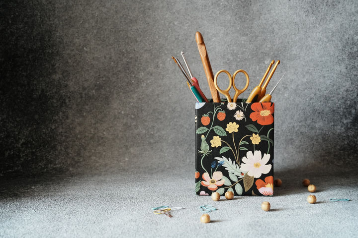 pencil holder with crochet hooks and yellow scissors on dark black background