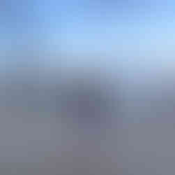 Eine junge Frau mit kurzer blauer Hose und schwarzes T-Shirt steht an einem Hafen mit Blick zum Leuchtturm. Der blaue Himmel ist von wenigen Wolken geprägt und taucht die Szene langsam rosa-orange.