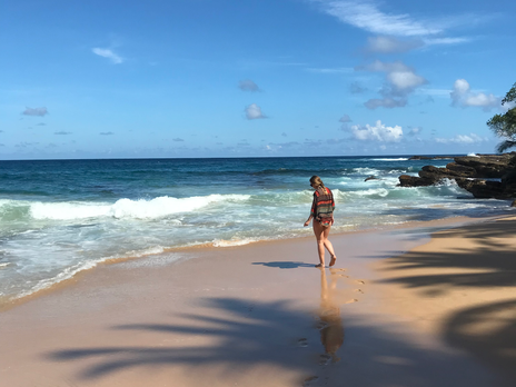 Eine junge Frau im bunten Hemd läuft einen menschenleeren Strand in Richtung Meer.