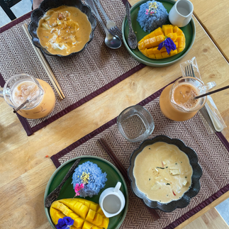 Aufnahme von oben: Zwei Sets mit schwarzen und grünen Tellern Tellern und wunderschön angerichteten Thai Gerichten. Dazu 2 Glaskaraffen mit gold braunem Thai Tee.