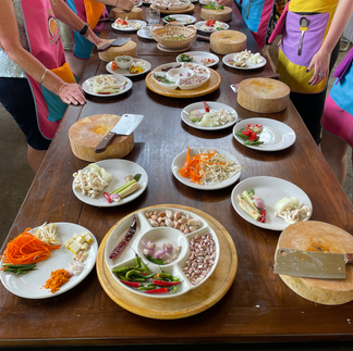 Auf einem braunen Holztisch befindet sich viele Teller und Brettchen mit klein geschnittenem Thai Essen.