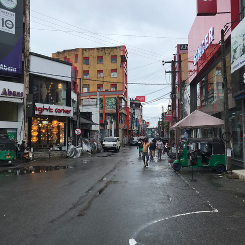 Eine nasse Straße, über die Stromkabel miteinander verbunden sind, ein paar Einwohner von Galle und Läden, in denen es leuchtet.