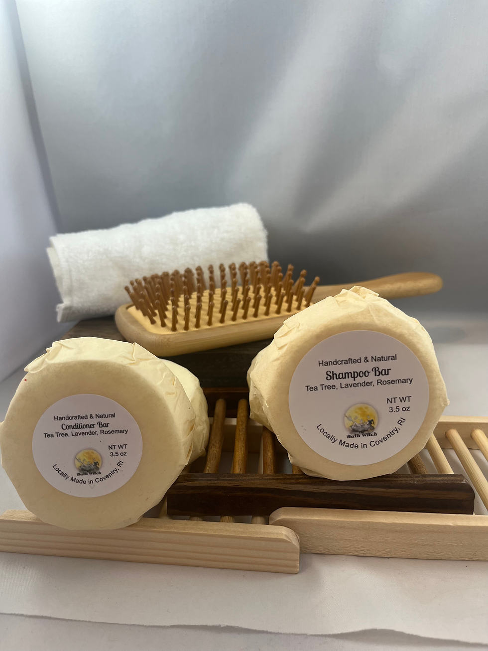 Thumbnail: Natural shampoo and conditioner bars wrapped in paper and set on wooden racks with a bamboo brush in the background.