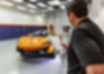 An over-the-shoulder view of Bill conducting a final quality control checklist inspection on a vibrant orange McLaren, which has been fully protected with SunTek Reaction PPF, in the clean, professional Immaculate Paint Protection shop.