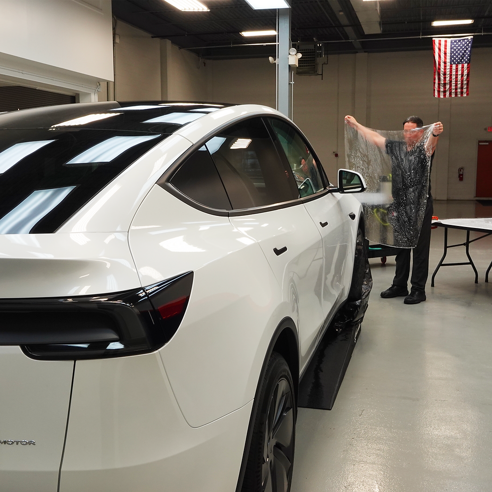 Bill Fetter of Immaculate Paint Protection holding up a large, pre-cut sheet of SunTek Paint Protection Film (PPF) for a Tesla Model Y hood, demonstrating the scale of the material before installation.