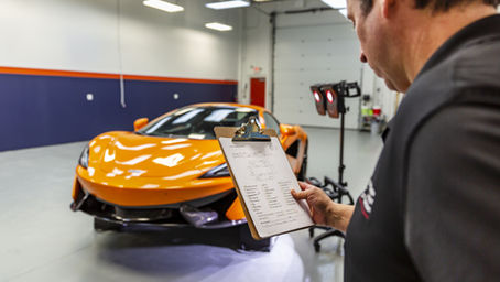 Bill Fetter of Immaculate Paint Protection holding a clipboard and performing a post-installation inspection on an orange 2020 McLaren 570S in his professional Allentown, PA paint protection studio.
