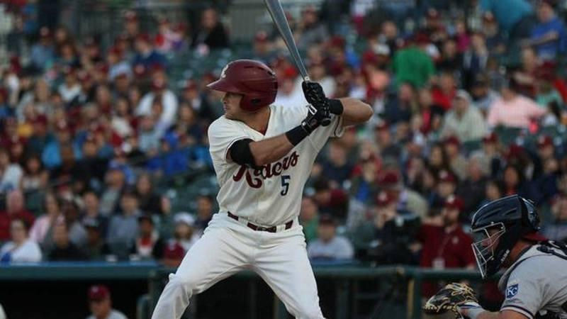 A baseball player wearing a white RoughRiders Jersey
