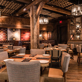 Interior of Haywire restaurant at Legacy West featuring rustic wood beams, Southwestern-style décor, cozy booths, and neatly set dining tables.