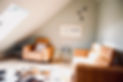 2 tan leather armchairs sit behind a sage coloured wall on a wooden floor beneath the eaves of a modern loft conversion.