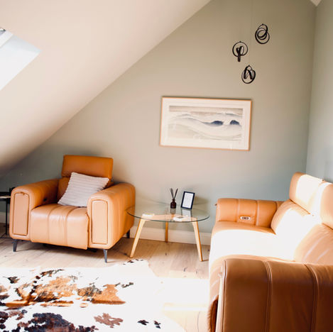 2 tan leather armchairs sit behind a sage coloured wall on a wooden floor beneath the eaves of a modern loft conversion.