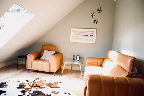 2 tan leather armchairs sit behind a sage coloured wall on a wooden floor beneath the eaves of a modern loft conversion.