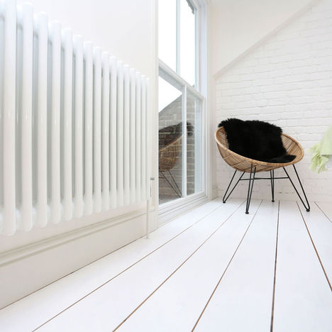 A low angle show showing a white wood floor, white radiator, the edge of a bed and a modern armchair which sits besides the new window and roof line of a recent loft conversion.