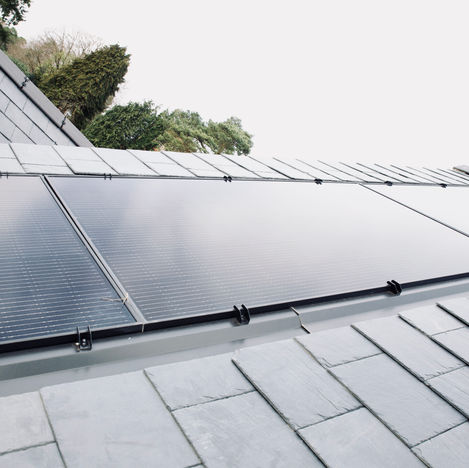 An outside image showing a dark slate tiled roof on white black solar panels have been installed.