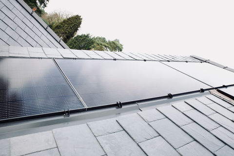 An outside image showing a dark slate tiled roof on white black solar panels have been installed.