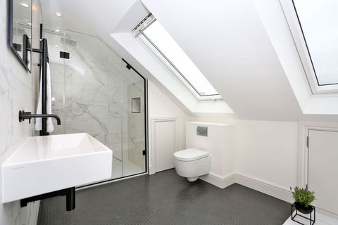 A large bathroom loft conversion shows a grey floor, marble tiled walk in shower, toilet and large skylight in a white roof.