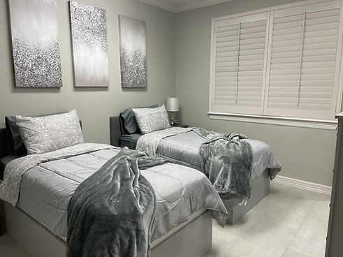 The New Canvas Recovery Brazilian Butt Lift Suite features two double beds with grey bedding and three panels of sparkly grey and silver art on the wall with large tile floors