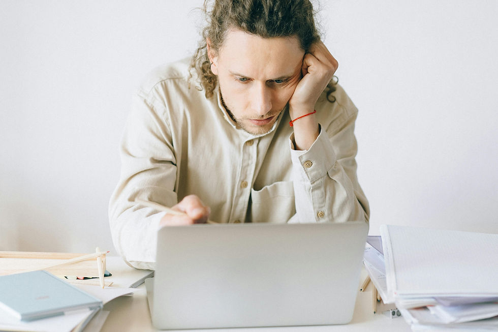 A person in a beige shirt looks focused at a laptop, surrounded by books and papers. The setting is a minimal, light-colored office space.