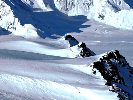 A massive, snow-covered mountain peak in the St. Elias Range with sharp ridges and deep blue shadows, representing the sharpened intuition required at the edge of the map.