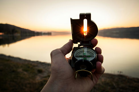 A hand holding a compass with the sun rays shinging through.