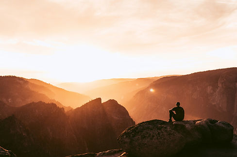 A man sitting on a rock, looking at the runrise.