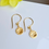 Thumbnail: Close up detail image of gold vermeil little flower drop earrings on hook ear wires.