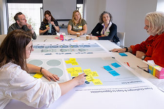 Women wearing glasses and black and white striped T-shirt writing on an orange post-it note on a large sheet of white paper with multiple post-its