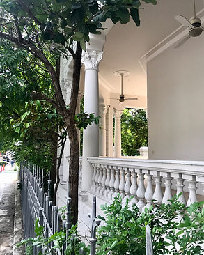 Elegant white veranda porch with Corinthian columns and stone balustrade railings next to a tree-line street.