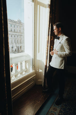 The groom gazing thoughtfully out a window at 116 Pall Mall, city life bustling on the street below.