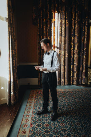 The groom standing by a window at 116 Pall Mall, reading a heartfelt letter from the bride, natural light highlighting the quiet moment.