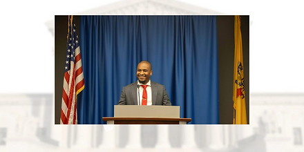 A man in a suit and tie stands confidently at a podium, preparing to address an audience.