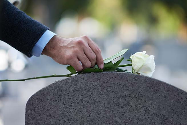 Hand Putting White Rose On Top Of Tombstone